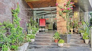 Entrada de hotel con escaleras de piedra, plantas en macetas y un cartel de bienvenida.