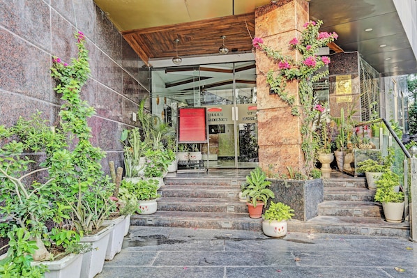 Entrada de hotel con escaleras de piedra, plantas en macetas y un cartel de bienvenida.