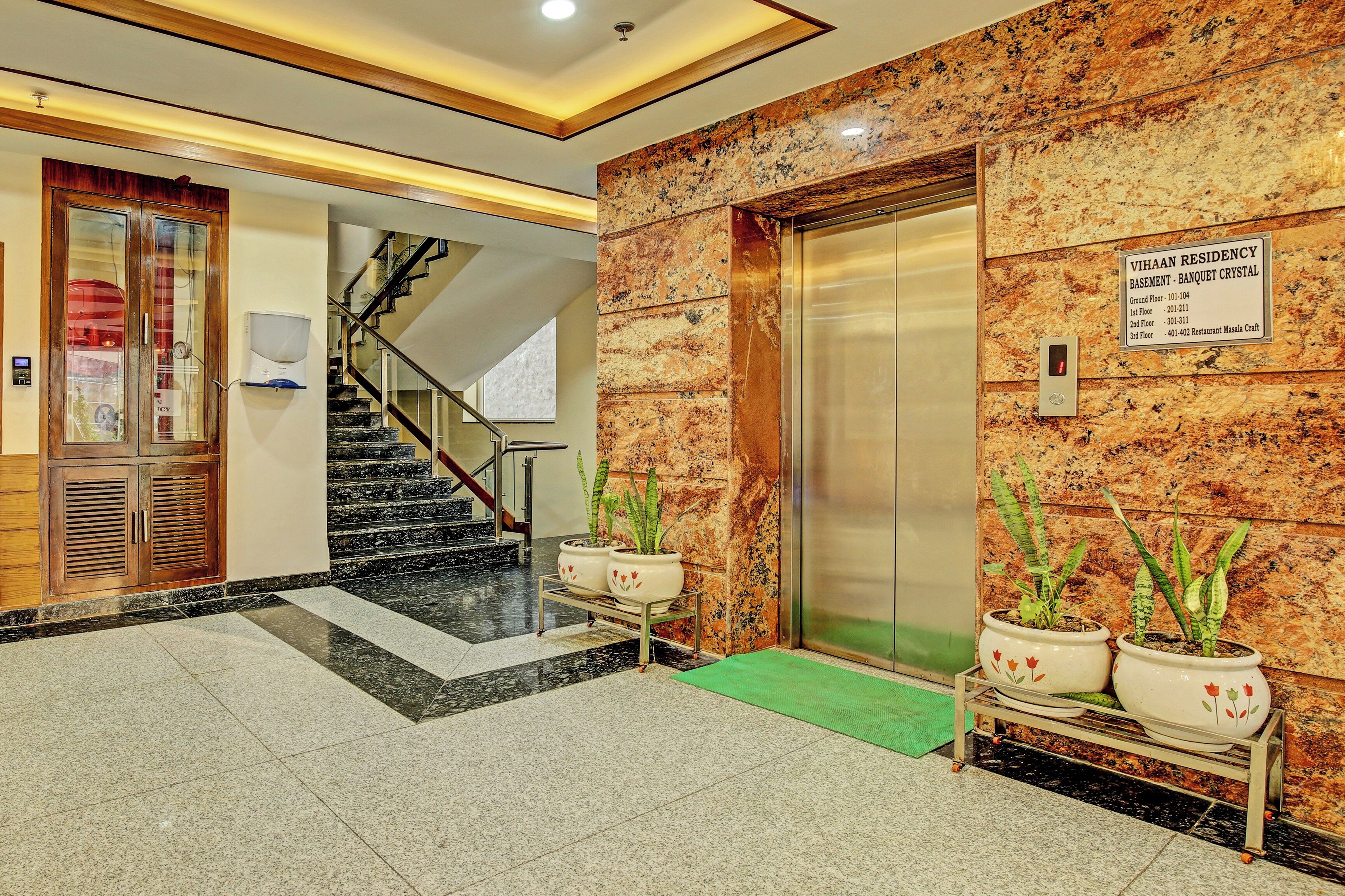 Un vestíbulo de hotel con piso de mármol, una escalera, un ascensor y una mesa de recepción.