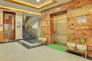 Rebedor d'hotel amb sòl de marbre, una escala, un ascensor i una recepció.