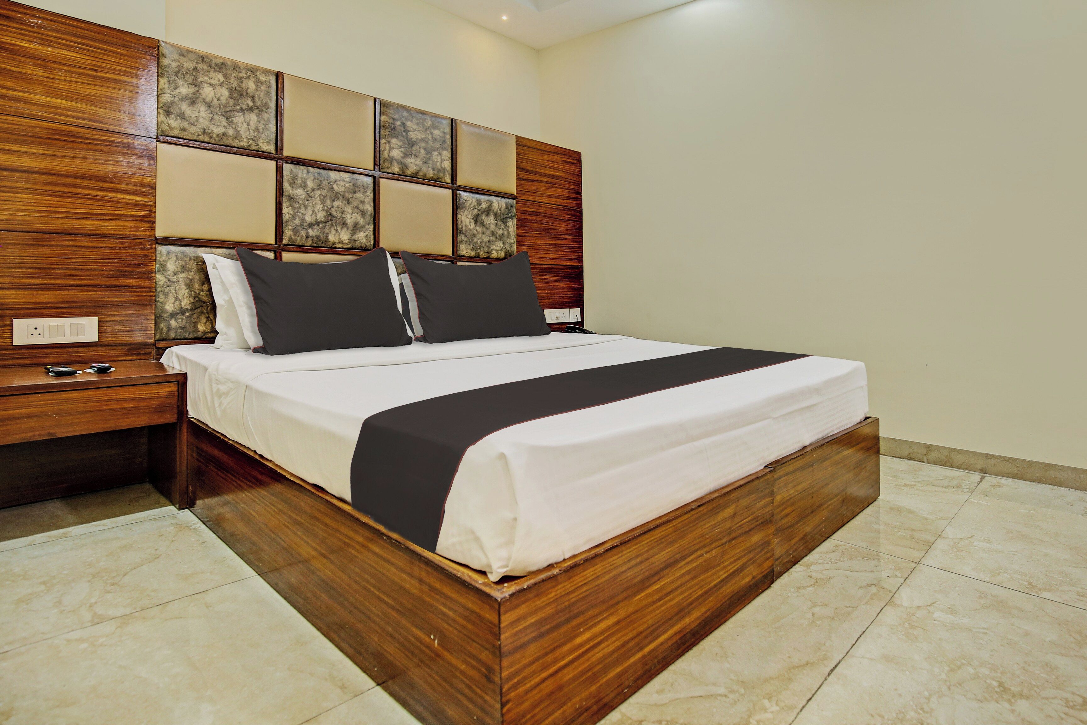 A modern bedroom with a wooden bed frame, a headboard with a geometric pattern, and a bedside table with a lamp.