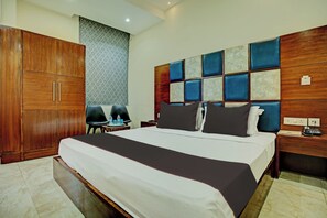 A hotel room with a large bed, a wooden wardrobe, a desk with a telephone, and a patterned wall. - Townhouse by OYO Eastern View (Zirakpur)