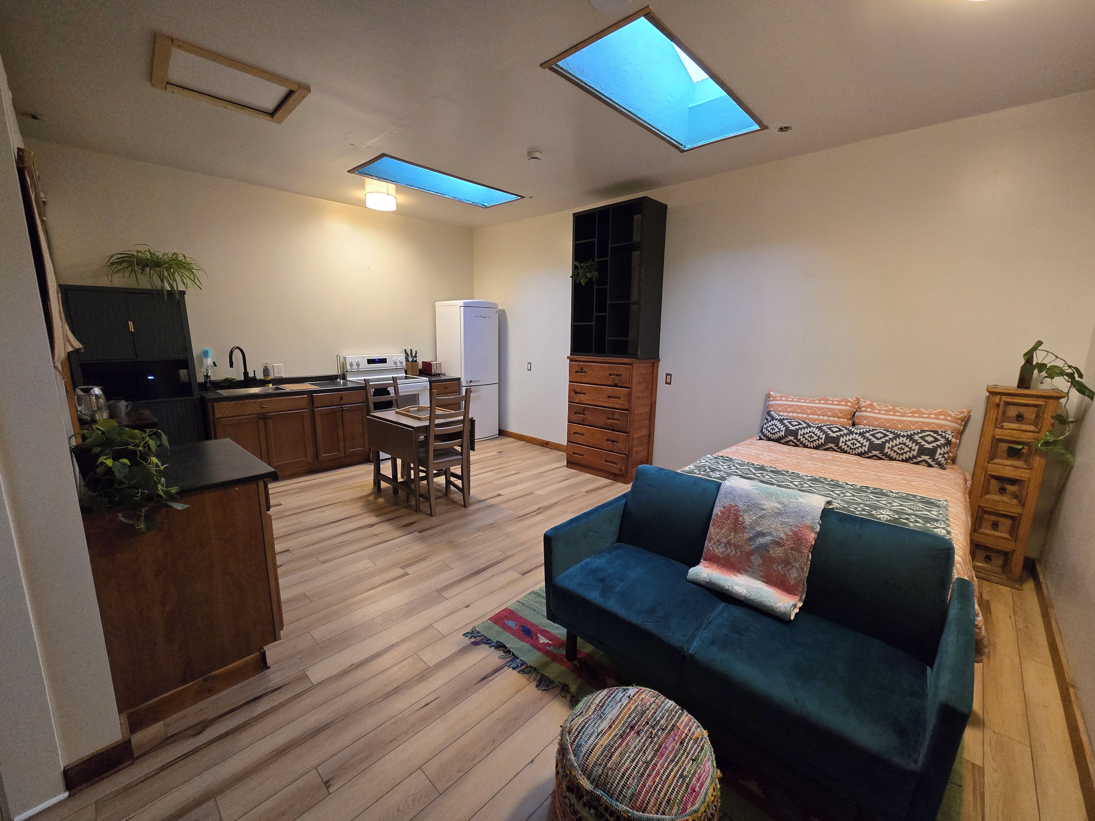 A compact living space with a kitchenette, a sofa, a dining table with chairs, and a bed with patterned bedding.