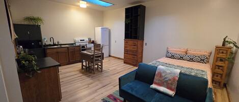 A compact living space with a kitchenette, a sofa, a dining table with chairs, and a bed with patterned bedding.