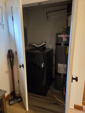 A laundry room with a large water heater, a vacuum cleaner, and a door leading to another room. - Cozy cottage close to skiing, hiking, and not far from downtown! (Murray)