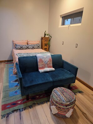 A bedroom with a bed, a sofa, a small table, and a window. - Cozy cottage close to skiing, hiking, and not far from downtown! (Murray)