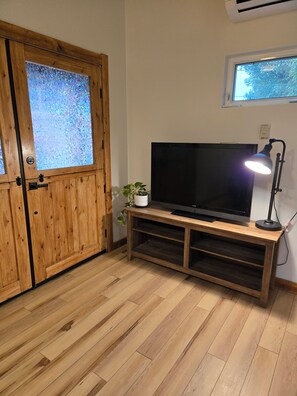 A room with a wooden door, a television on a wooden stand, a potted plant, and a window. - Cozy cottage close to skiing, hiking, and not far from downtown! (Murray)