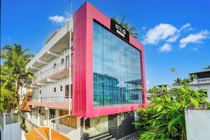 A modern hotel with a prominent glass facade, a red and white exterior, and a sign indicating it is a company-serviced hotel.