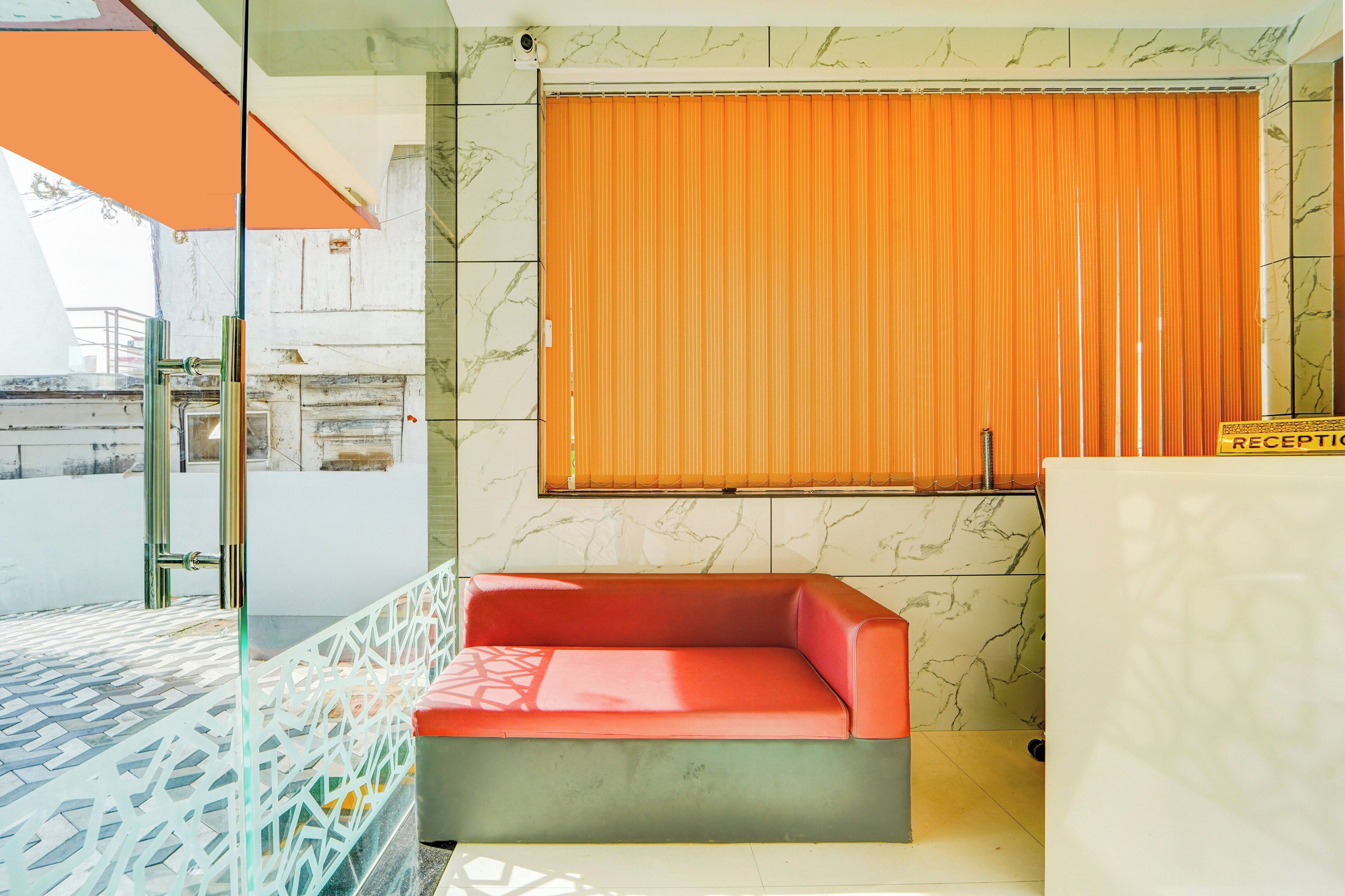 A hotel room with a red sofa, a reception desk, and a window with orange curtains.