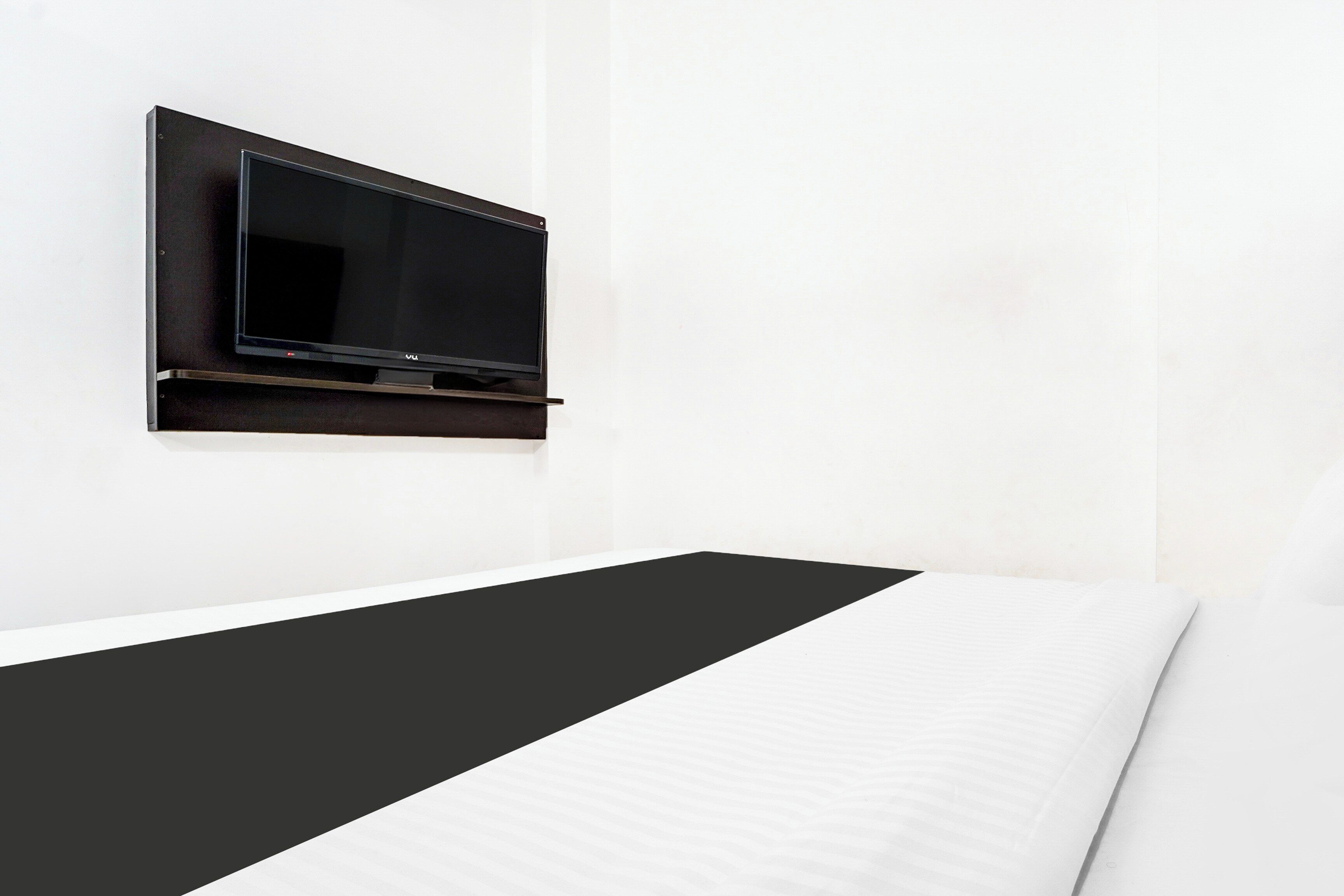 Una cama individual con colcha a rayas blancas y negras, un televisor de pantalla plana montado en la pared y una pared blanca lisa.