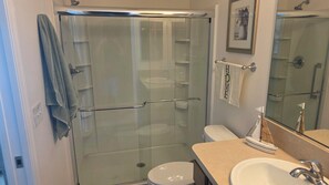 A bathroom with a glass-enclosed shower, a toilet, a sink, and a mirror. - Cozy 2-bedroom house in the villages. (Wildwood)