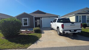 A residential driveway with a white GMC truck parked in front of a house with a garage. - Cozy 2-bedroom house in the villages. (Wildwood)