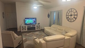 A living room with a television, a sofa, a chair, a rug, and a clock on the wall. - Cozy 2-bedroom house in the villages. (Wildwood)
