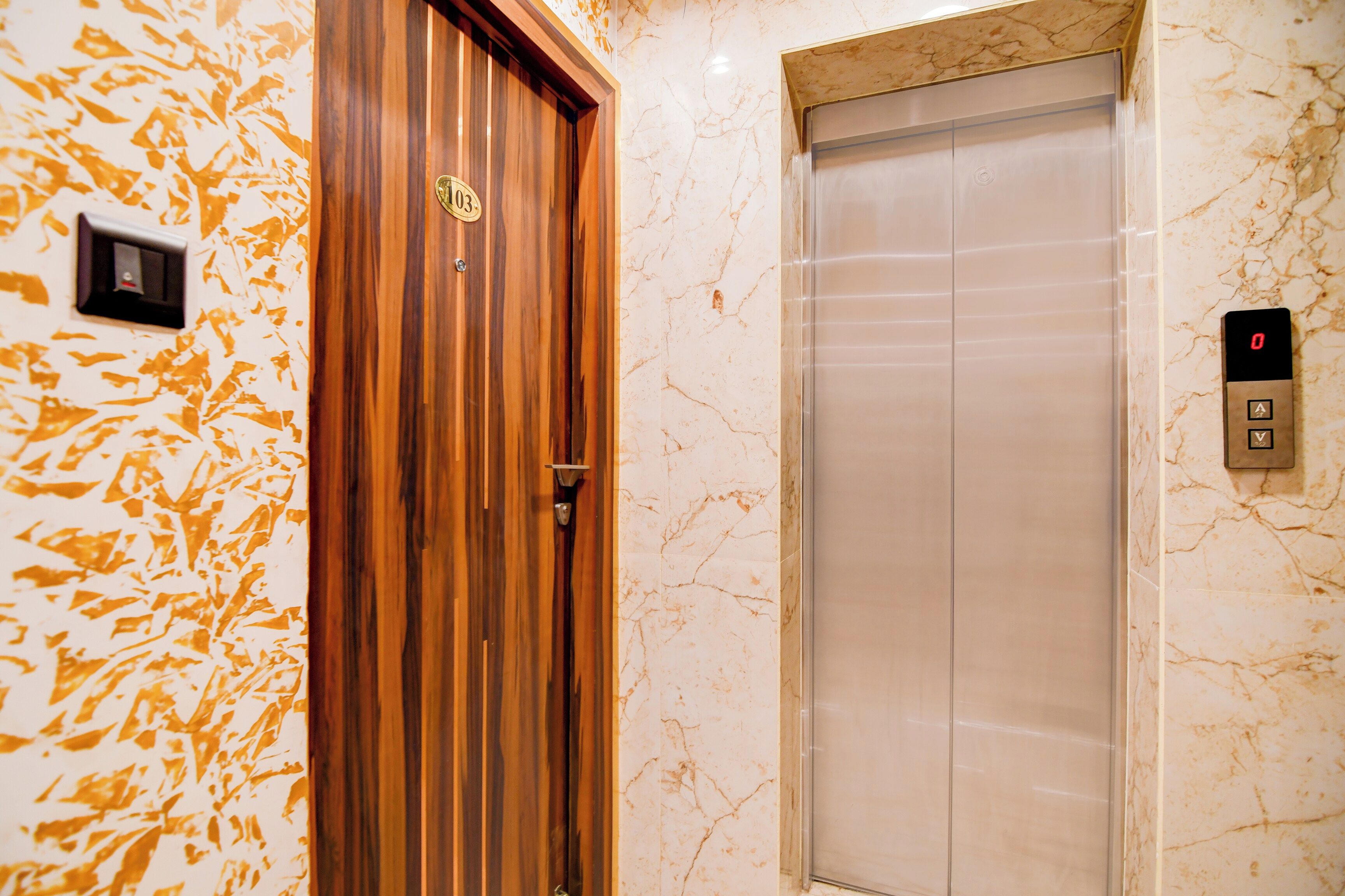 An elevator with a marble wall and a wooden door with a brass handle.