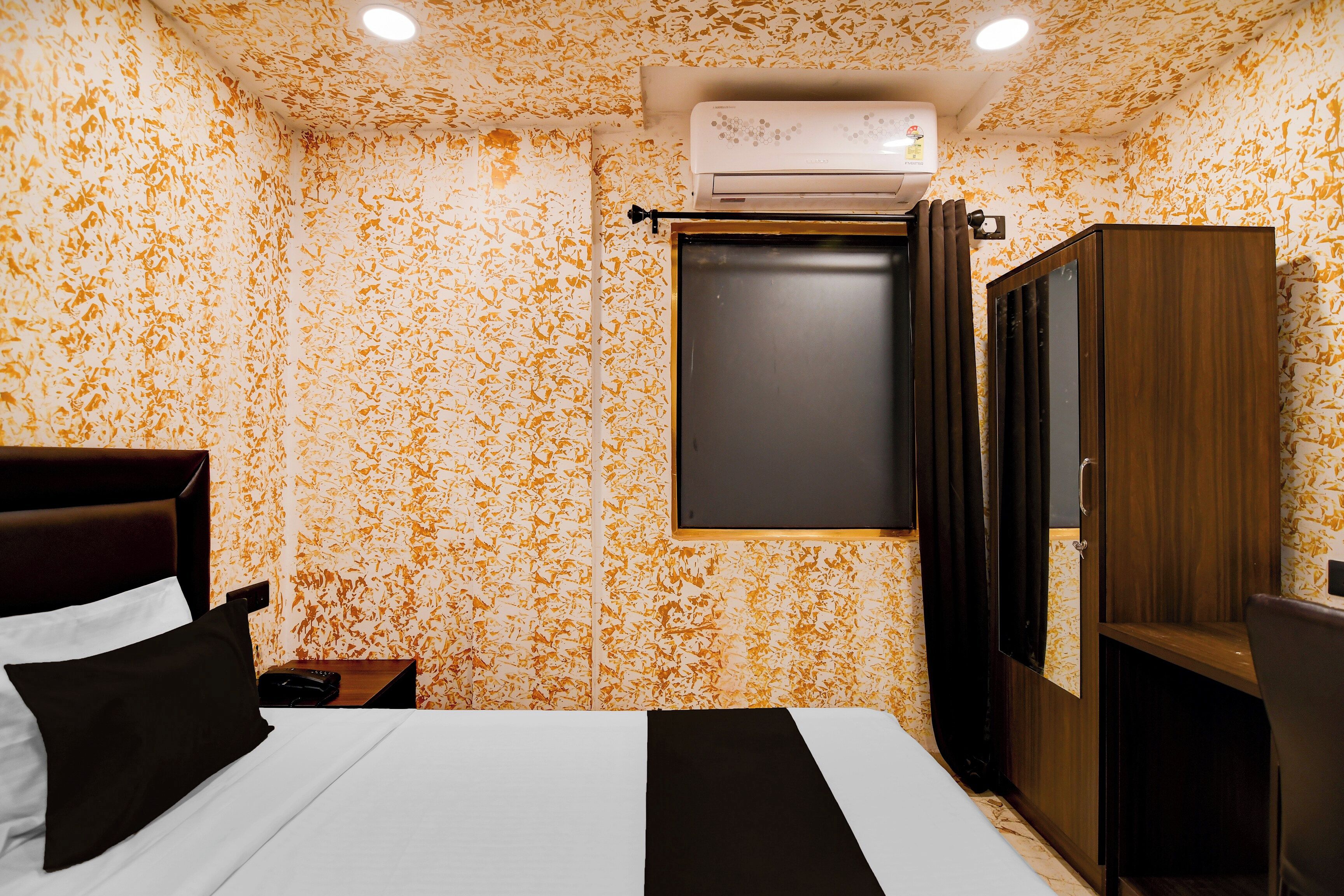 A hotel room with a bed, a nightstand, a wardrobe, and an air conditioning unit.