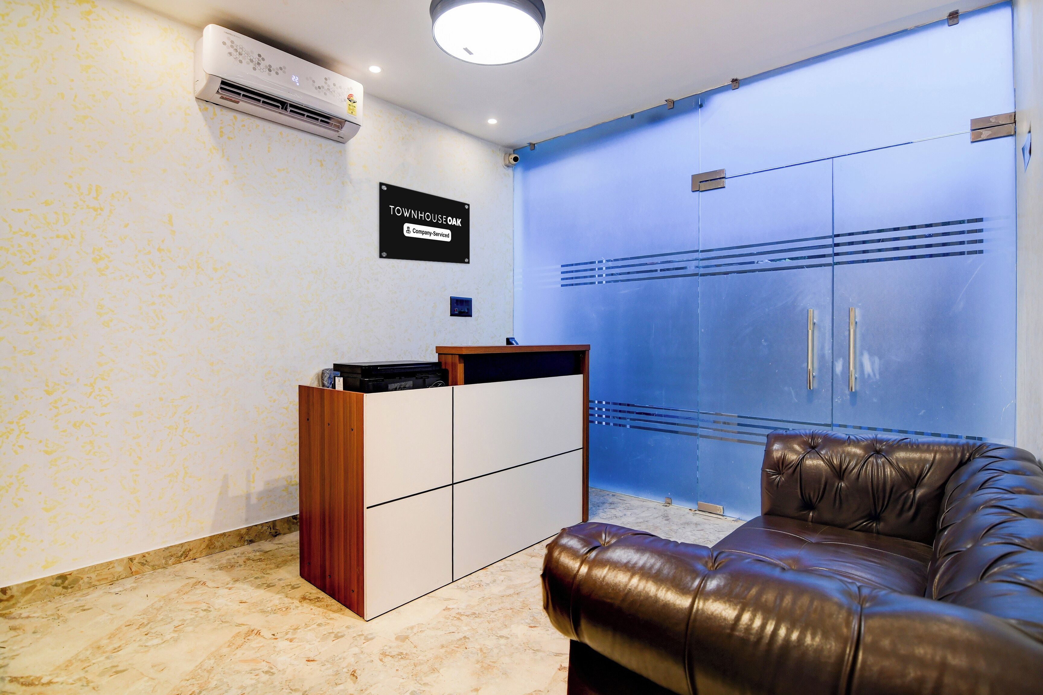 Un área de recepción con un escritorio de madera, un sofá de cuero y un aire acondicionado instalado en la pared.