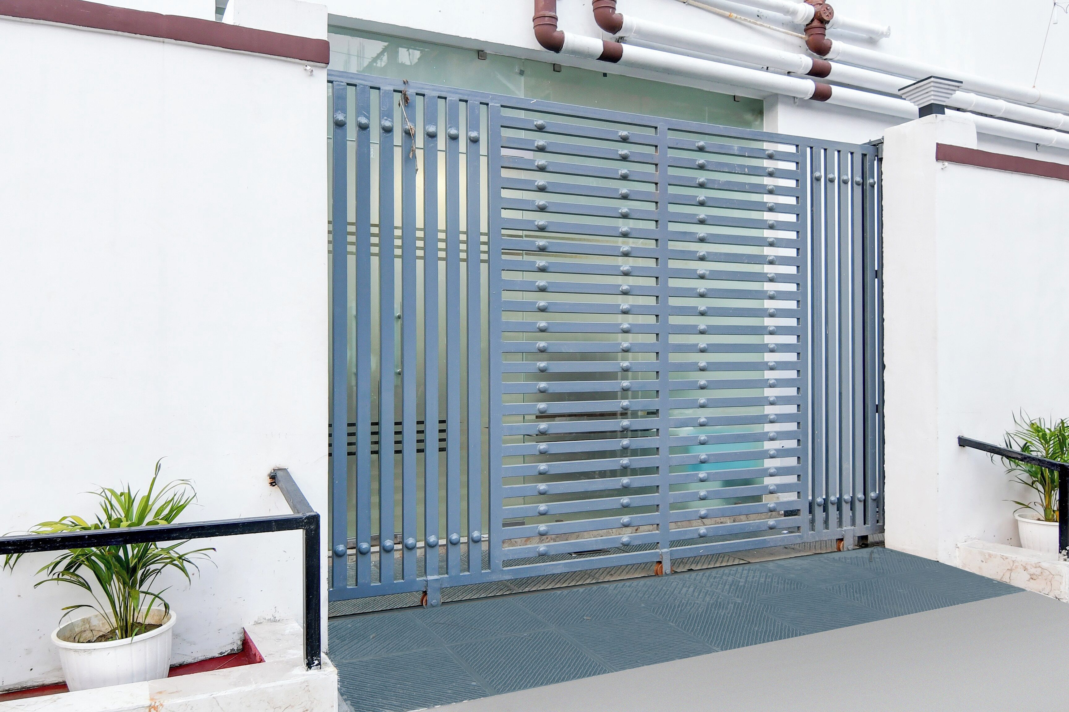 A metal gate with horizontal slats, a potted plant to the left, and a potted plant to the right.