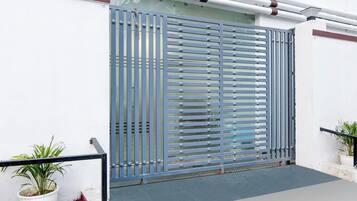 A metal gate with horizontal slats, a potted plant to the left, and a potted plant to the right.