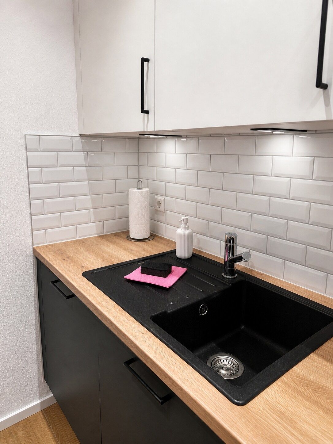 Een keuken met een zwart spoelbak, een houten aanrechtblad en een witte betegelde achterwand.