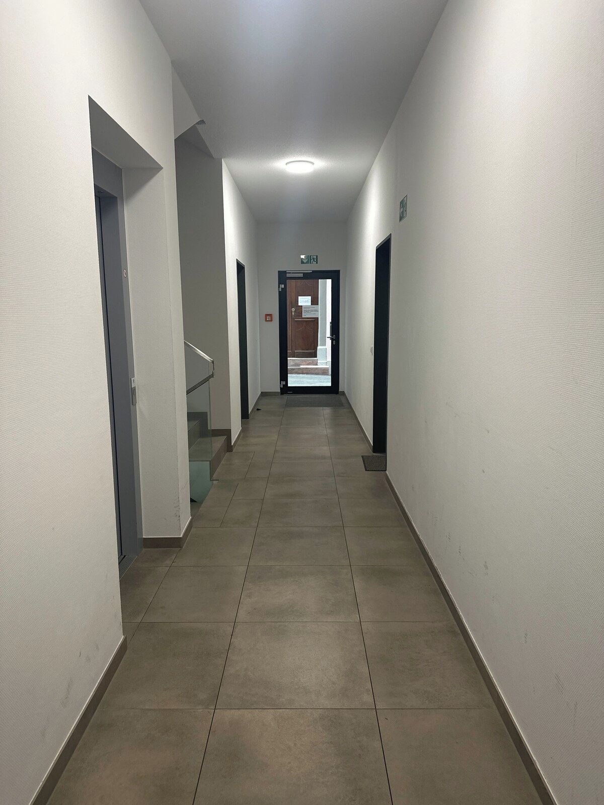 Ein Korridor mit Fliesenboden, weißen Wänden und einer Tür am Ende, die zu einer Treppe führt.