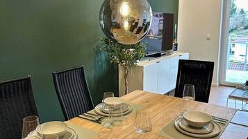 A dining area with a wooden table set for four, surrounded by black chairs, and a green wall in the background.