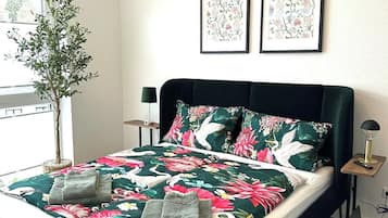 Ein Bett mit einer blumigen Tagesdecke, einer Nachttischlampe und einem Blumentopf.