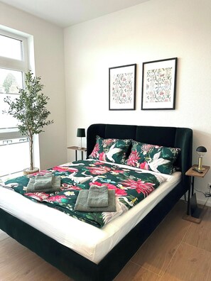 Ein Bett mit einer blumigen Tagesdecke, einer Nachttischlampe und einem Blumentopf.