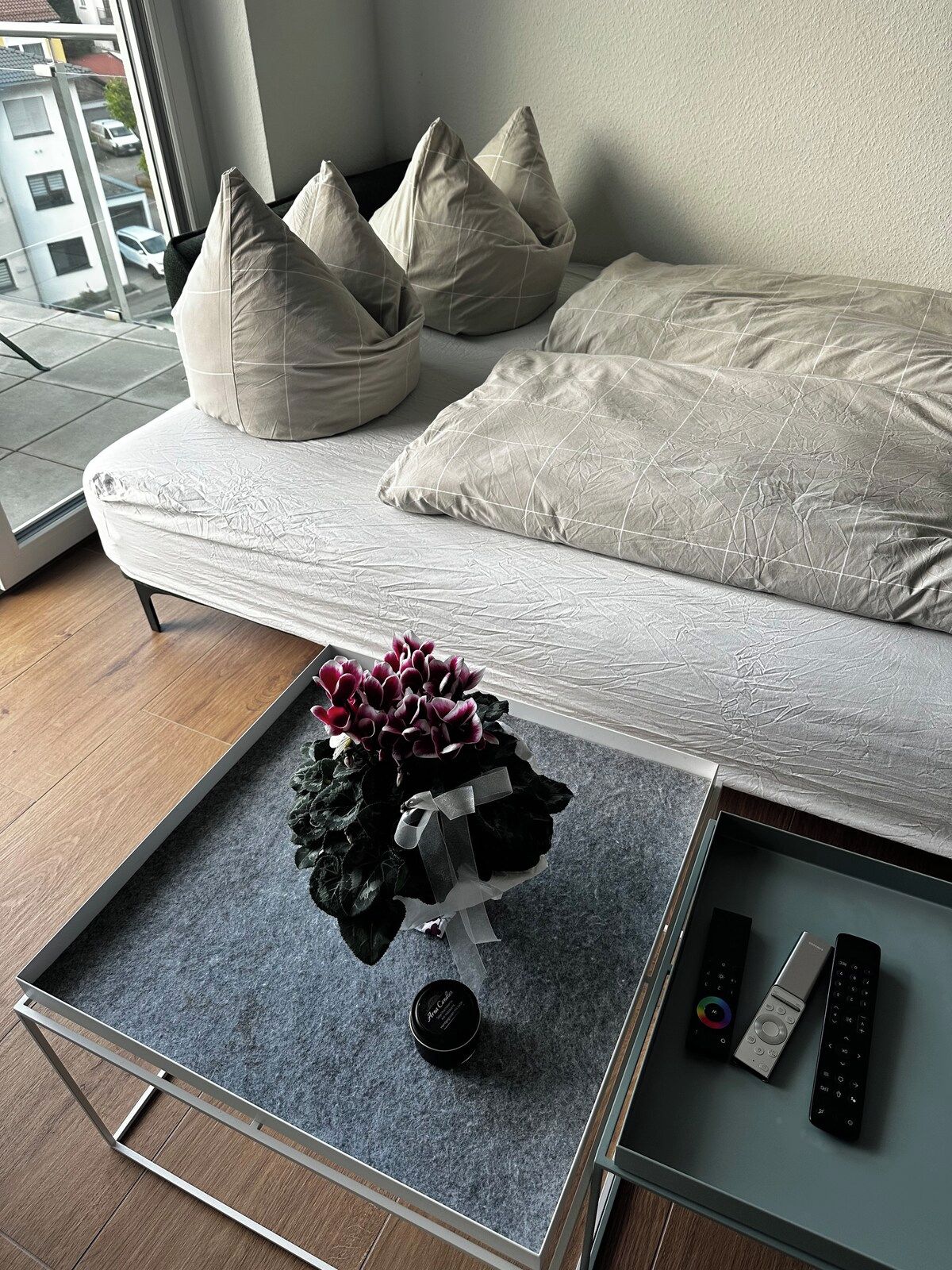 Ein modernes Schlafzimmer mit Bett, Kissen, einem kleinen Tisch mit Pflanze und Fernbedienungen.