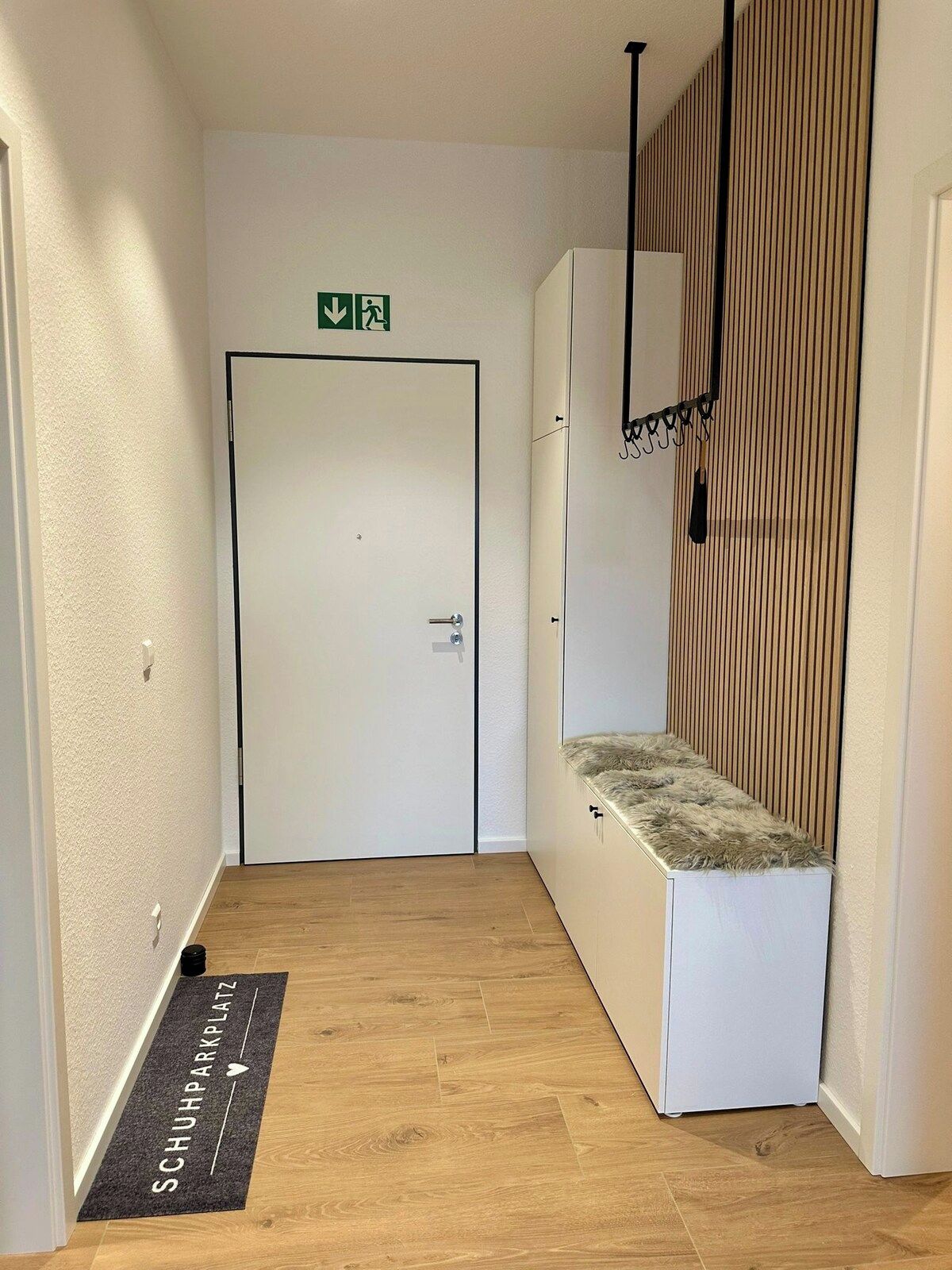 A hallway with a white door, a bench with a fur-like texture, and a doormat with text.