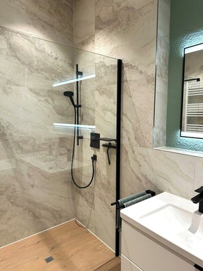 Ein modernes Badezimmer mit einer gläsernen Dusche, einem weißen Waschbecken und einem Spiegel darüber.