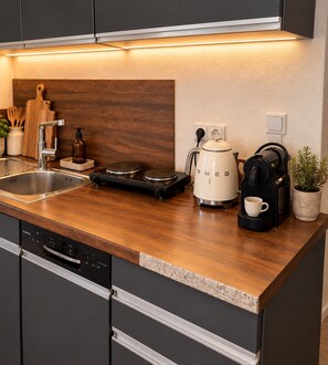 A kitchen with a wooden countertop, a coffee maker, a kettle, and a dishwasher. - STAY | Easy Apartment, Parkplatz, Bodensee (Friedrichshafen)