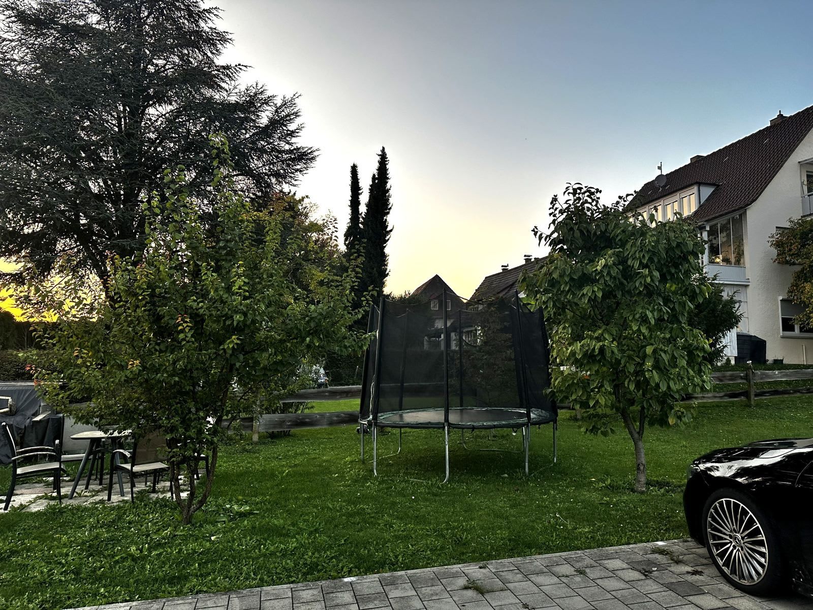 A residential area with a trampoline in a yard, surrounded by trees and a house.