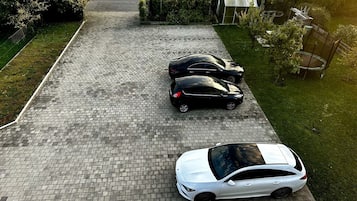 A paved driveway with three parked cars, a grassy area, and a hedge.