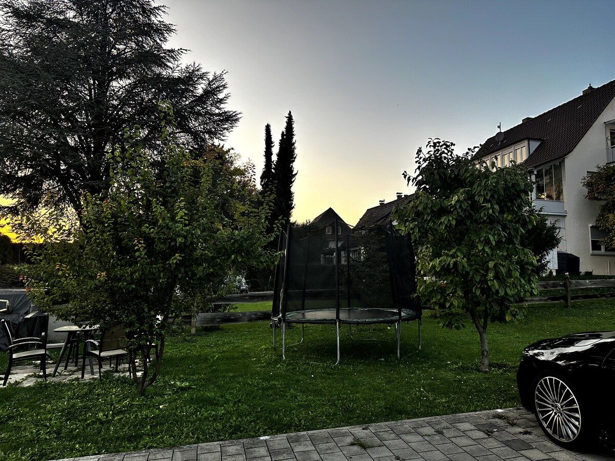 A residential area with a trampoline, trees, and a parked car.