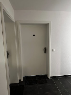 En vit dörr med en liten ventil, ett dörrhandtag och en ljusströmbrytare på väggen till höger.
