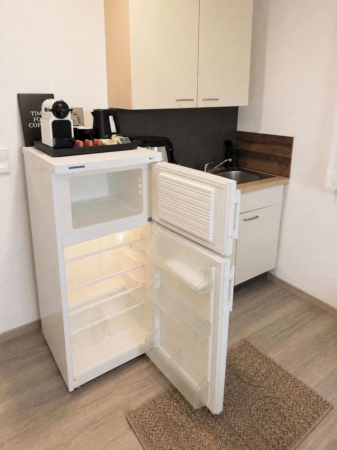 A compact kitchen with a built-in refrigerator, a coffee maker, and a sink.