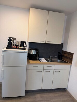 Eine kleine Küche mit Kühlschrank, Kaffeemaschine, Wasserkocher und Spüle.