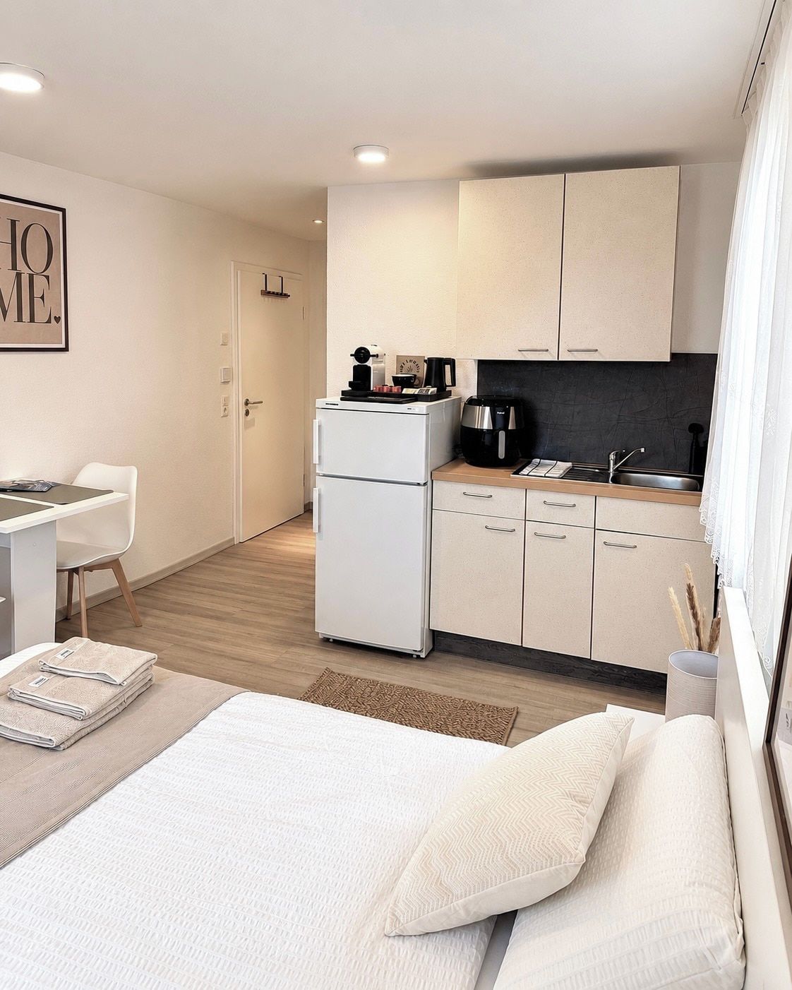 Quarto de hotel moderno com cama, escrivaninha, cozinha compacta e banheiro.
