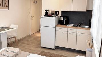 Quarto de hotel moderno com cama, escrivaninha, cozinha compacta e banheiro.