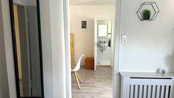Ein Flur, der zu einem Badezimmer mit einem weißen Heizkörper, einem weißen Stuhl und einer sechseckigen Wanddekoration führt.
