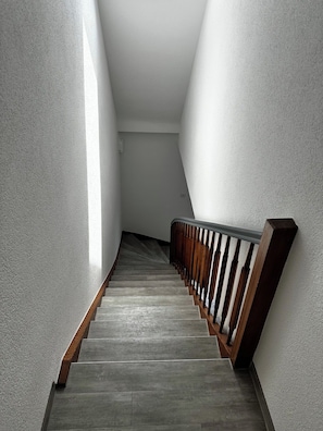 A staircase with a wooden handrail and a grey floor. - STAY | City-Apartment W32, Friedrichshafen (Friedrichshafen)