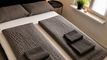 A modern bedroom with a large bed, a bedside table, a lamp, and a window with a view of greenery.