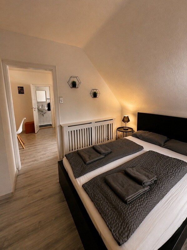 A bedroom with a large bed, a bedside table with a lamp, and a view of a bathroom. - STAY | City-Apartment W32, Friedrichshafen (Friedrichshafen)