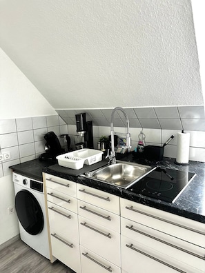 A compact kitchen with a built-in washing machine, a sink, and a stove. - STAY | City-Apartment W32, Friedrichshafen (Friedrichshafen)