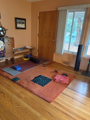 Ein Zimmer mit Holzboden, einer Yogamatte, einem blauen Trainingswürfel, einem rosa Handtuch und einer Tür mit Blick ins Freie.