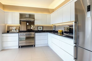 A modern kitchen with stainless steel appliances, white cabinetry, and a black countertop. - Milkwood Sanctuary, 6-Bed Home in Hermanus (Hermanus)