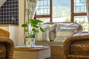 A wicker sofa with patterned cushions, a potted plant, and a tray with a lid. - Milkwood Sanctuary, 6-Bed Home in Hermanus (Hermanus)