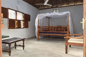 A room with a wooden four-poster bed, a small table, and a chair.