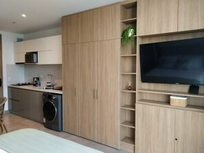 Une cuisine moderne dotée d’appareils électroménagers intégrés, de meubles en bois et d’un téléviseur à écran plat posé sur une étagère en bois.