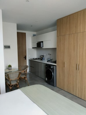 A compact kitchen with a microwave, stove, and washing machine. There is a dining area with a table and chairs. - New Studio Steps from Santa Marta Marina & Beach - A/C, Washer-Dryer (Santa Marta)